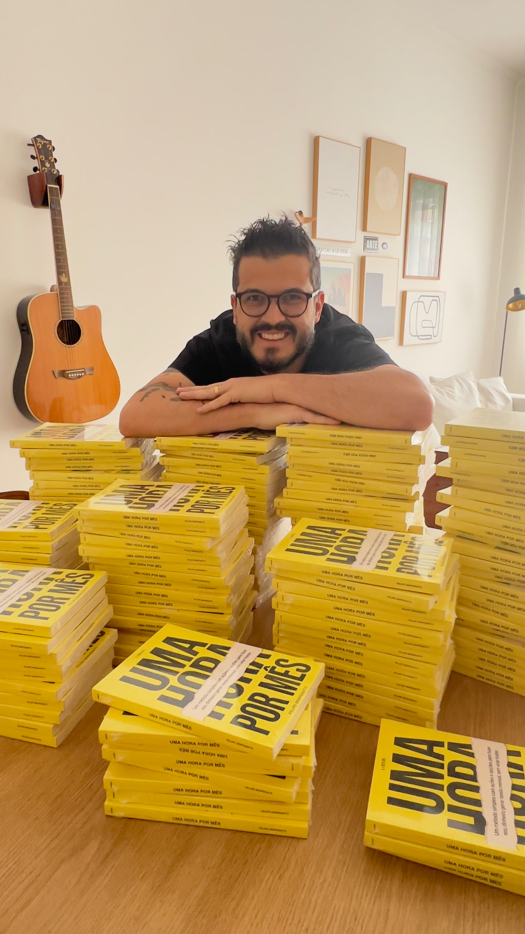 Felipe Benfenatti apoiado sobre pilhas de exemplares impressos do livro Uma Hora por Mês